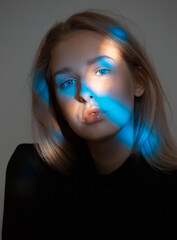 Fashionable beauty portrait of young girl posing in studio. Girl with blue light on her face