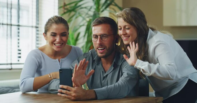 Authentic shot of young happy college friends are making a selfie or video call to relatives or friends with smartphone in a living room at home.
