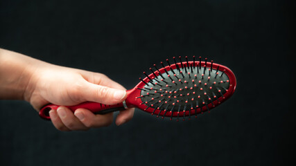 Woman's hand on black background holding red hairbrush	