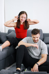 Smiling young Caucasian couple love is listening to online music with Headphones and laptop together on sofa in living room. Lifestyle and relationship of married life on holiday Concept.