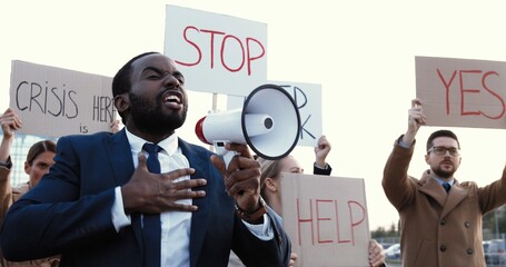 African American handsome man in suit and tie talking in megaphone outdoor at protest against...
