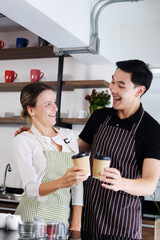Smiling young barista couple loves Asian man and caucasian woman is hugging and  holding cups of hot coffee together. Start up Coffee shop and cafe business concept.