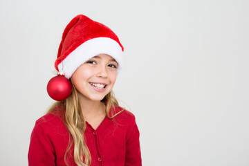Young smiling girl in red santa hat with christmas ball. Child with Christmas decoration, banner copy space. Isolated on white background.