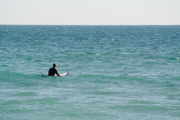 Hombre de espaldas con traje de neopreno practicando surf, esperando la ola
