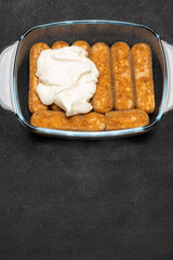 tiramisu dessert cooking - Traditional Italian Savoiardi ladyfingers Biscuits and cream in glass baking dish on dark concrete background