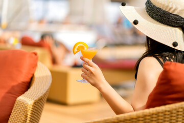 close up young woman holds a glass of tropic cocktail orange margarita and piece of orange having...