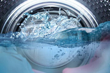 Washing machine drum with water and clothes, closeup view