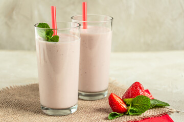delicious milkshake with strawberries in tall glasses, strawberries and mint, burlap napkin create a cozy atmosphere