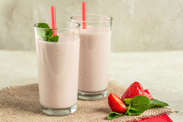 delicious milkshake with strawberries in tall glasses, strawberries and mint, burlap napkin create...