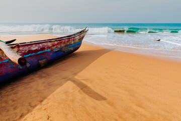 Obraz premium Beautiful morning over Sri Lanka sandy ocean beach. Traditional fisherman's boat on a coast in front of turquoise ocean waves.