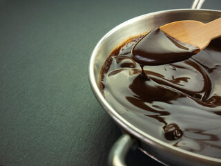 Melting chocolate, drop of hot chocolate on wooden spoon close up, spoon full of melted chocolate,...