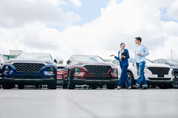 Positive female car dealership saleswoman walking along rows of new cars with customer