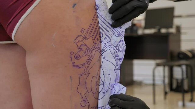 Tattoo artist puts a picture on the leg of a woman, the process of creating a tattoo. Close-up.