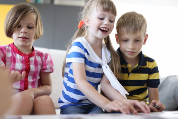 Two girls and boy sit side by side on couch. Happy girl take playing card from table.