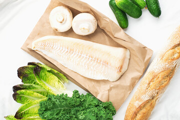 Cod simple healthy food ingredients: white fish, vegetables, mushrooms, green leafy salads, onions, cabbage, kale, hot peppers on a light background. Flat lay. Top view.
