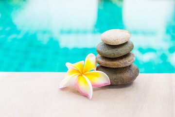 Fototapeta na wymiar Beautiful stone stack with fresh Plumeria flower on swimming pool edge with space on blurred blue background, spa background idea, outdoor day light
