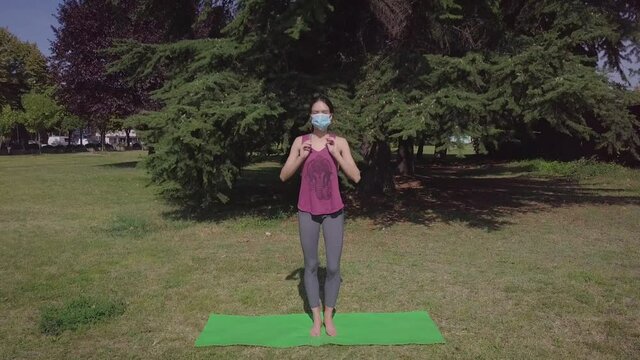 Caucasian girl putting mask and doing namaste yoga position in the park