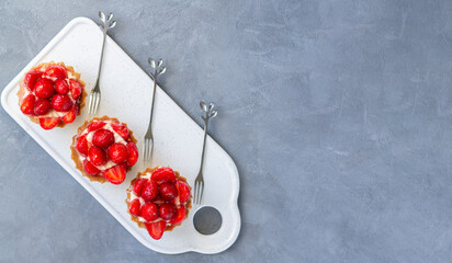 Three delicious strawberry tartlets with cream cheese on ceramic board top view