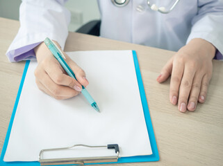 doctor in gown and stethoscope writing on patient chart on wooden table at hospital or clinic. worker or professional concept.