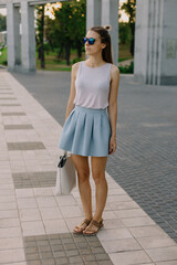 Beautiful and fit full-length girl in sunglasses and short skirt looking away. 