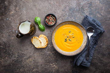 Vegetarian autumn pumpkin cream soup with seeds on dark background, top view