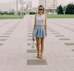 Fashion girl in summer light clothes and glasses standing on the street in summer day. 