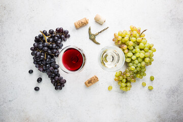 Fototapeta premium Glasses of white and red wine with ripe grapes on stone background, top view
