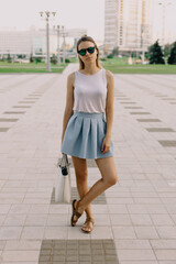 Fashion blogger walking in summer light clothes and glasses standing on the street in summer day.	
