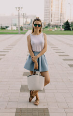 Pretty stylish girl in glasses and skirt smiling in camera. Big city background.
