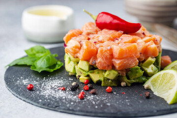 Delicious avocado and raw salmon salad, tartare, served on a black plate with lime, light background