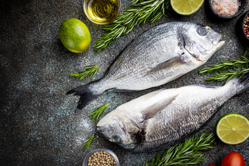 Fresh ready to cook raw bream fish dorado with ingredients and seasonings like rosemary, salt, pepper, lime and olive oil, top view