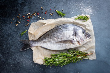 Fresh ready to cook raw bream fish dorado with ingredients and seasonings like rosemary, salt, pepper, lime and olive oil, top view