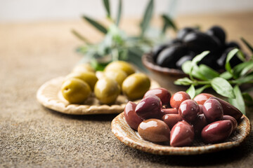 Variety of black and green olives and olive oil in bowls on stone background close up