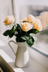 Bouquet pale pink cream roses in white jug on 
windowsill. Light background	