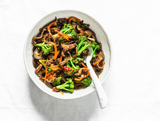 Stir fried beef with broccoli, carrots and chili peppers  on a light background, top view