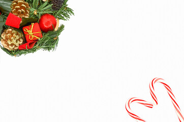Сhristmas background: decorations with fir branches, red gift boxes and ribbons in the left corner and striped candy canes folded in the shape of a heart in the right corner on white background.