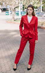 Beautiful girl in red business suit standing on the street. Long hair, smile. Business lady
