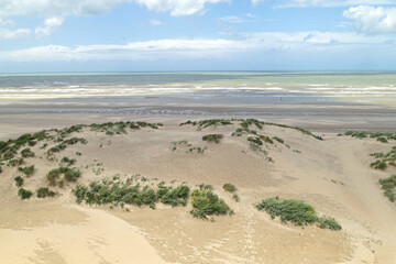 Panorama view over the beautiful dunes with green grass and the beach at low tide to the sea on a beautiful but windy day after rainfall
