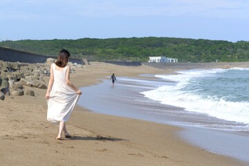 海岸を散歩する白いワンピース姿の若い女性