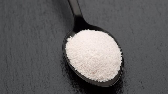 collagen powder in black spoon on black stone, rotating. Natural beauty and health supplement