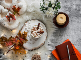 Cozy autumn still life - hot chocolate with marshmallows, garland, maple leaves, soft slippers on a fluffy carpet, top view