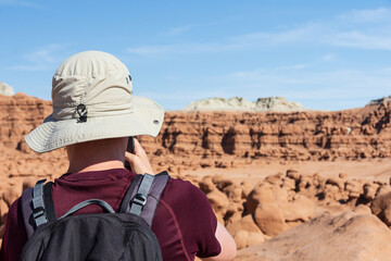 Young man with a hat and a backpack taking a picture of rock formations in a summer, sunny, day - Goblin Valley State Park, UT - USA