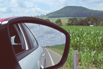 Espejo retrovisor del coche con el reflejo del lateral del mismo. Conduciendo por la carretera E60 entre los campos de cultivo de Transilvania, Rumanía.