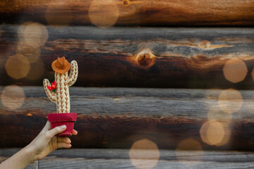 A hand holding the felt toy Cowboy cactus  with hat is on the old wooden texture background with yellow bokeh. Concept father's day, creative Christmas card. Copy space.
