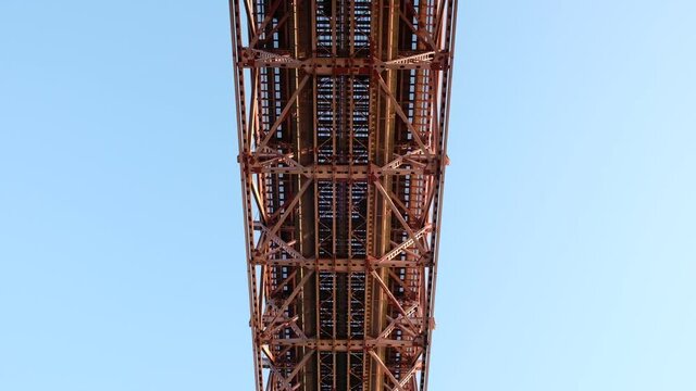 Red bridge shot from bellow with passing cars. Below double deck 25 de Abril Bridge over Tagus/Tejo river. Overhead shot of traffic in Lisbon.