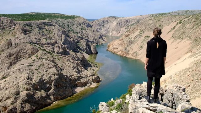 Girl in a black dress enjoying the breathtaking view of the Zrmanja canyon in Croatia. Sense of freedom travelling in Europe on the top of the canyon overlooking still turquoise water.