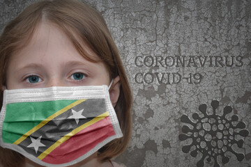 Little girl in medical mask with flag of saint kitts and nevis stands near the old vintage wall with text coronavirus, covid, and virus picture. Stop virus concept