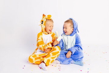 two little brother boys in bright costumes on a white isolated background eat ice cream and indulge, children's birthday, place for text