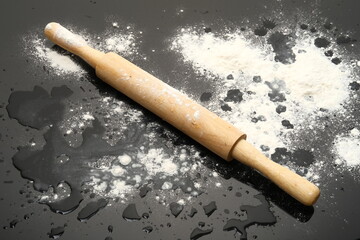 Rolling pin on a black glossy surface next to sprinkled flour and water drops
