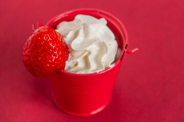 appetizing dessert in a red bucket on a red background, unusual table setting, whipped cream with strawberries